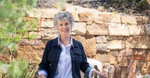 Woman wearing a white linen blouse and jean jacket sitting in front of a natural stone wall in Santa Fe, NM. If you're struggling to find comfort & hope in the midst of grieving, the Santa Fe Therapist can help. Online therapy in New Mexico. 87506, 87048, 87501, 87505, 87501, 87122, 87506, 87048, 87544