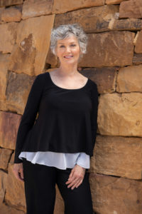 Santa Fe therapist standing in front a rust-colored dry stacked wall in Santa Fe NM. Grief & the holidays can feel especially difficult. The Santa Fe Therapist offers online grief counseling. Listen to the podcast here. 87505, 87506, 87508