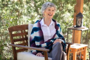 laughing woman sitting in wooden chair outside on her New Mexico portal. Stress management counseling with the Santa Fe Therapist. 87544, 87540, 87501, 87048, 87506