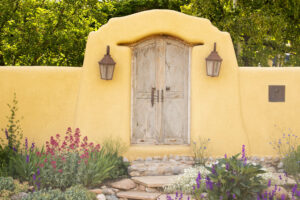 Soft yellow adobe fence with an graceful arch over a closed wooden doorway; 2 lanterns on either side of the doorway and flowering plants blooming next to stone steps. When your emotional health and wellbeing are strong, your life is vibrant and rich. The Santa Fe Therapist offers counseling for anxiety, stress, depression, grief, and trauma. 87122, 87506, 87048, 87501