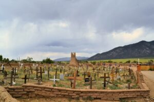 old cemetery with low adobe wall in Taos NM, with a cloudy sky and mountains. Dealing with sadness & loss can be challenging. Read the Santa Fe Therapist blog post on emotional healing in Santa Fe, NM and throughout New Mexico with online therapy. 87048, 87501, 87506, 87122